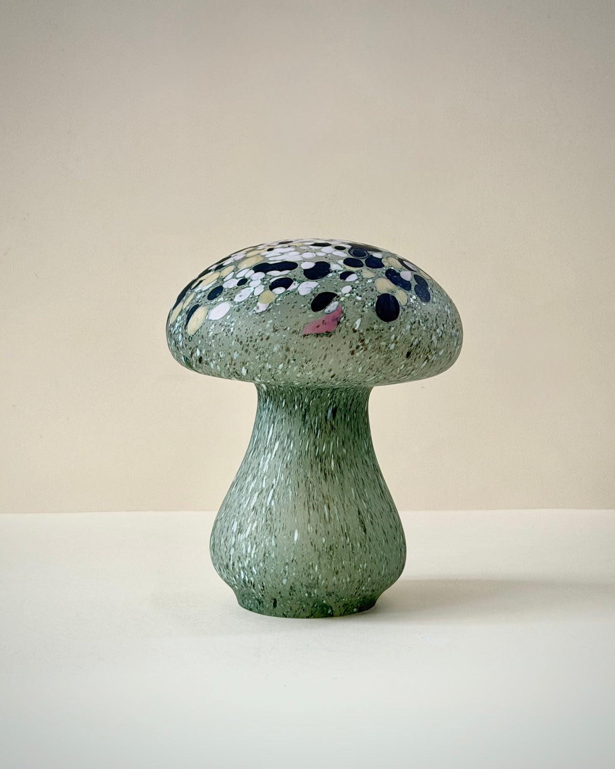 Close-up of the mushroom cap showing black, white, pale pink and warm yellow glass fragments in the translucent green glass.
